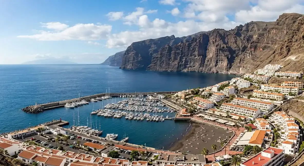 A breathtaking view of Los Gigantes resort in Tenerife, showcasing the massive volcanic cliffs, marina, and seaside hotels for travellers booking an affordable airport taxi transfer.