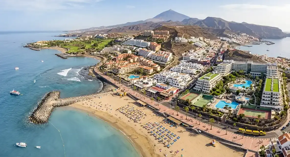 A vibrant view of Playa de las Americas resort in Tenerife, showcasing its lively nightlife venues, palm-lined shopping avenues, and sunny beaches for holidaymakers booking an affordable airport taxi transfer.