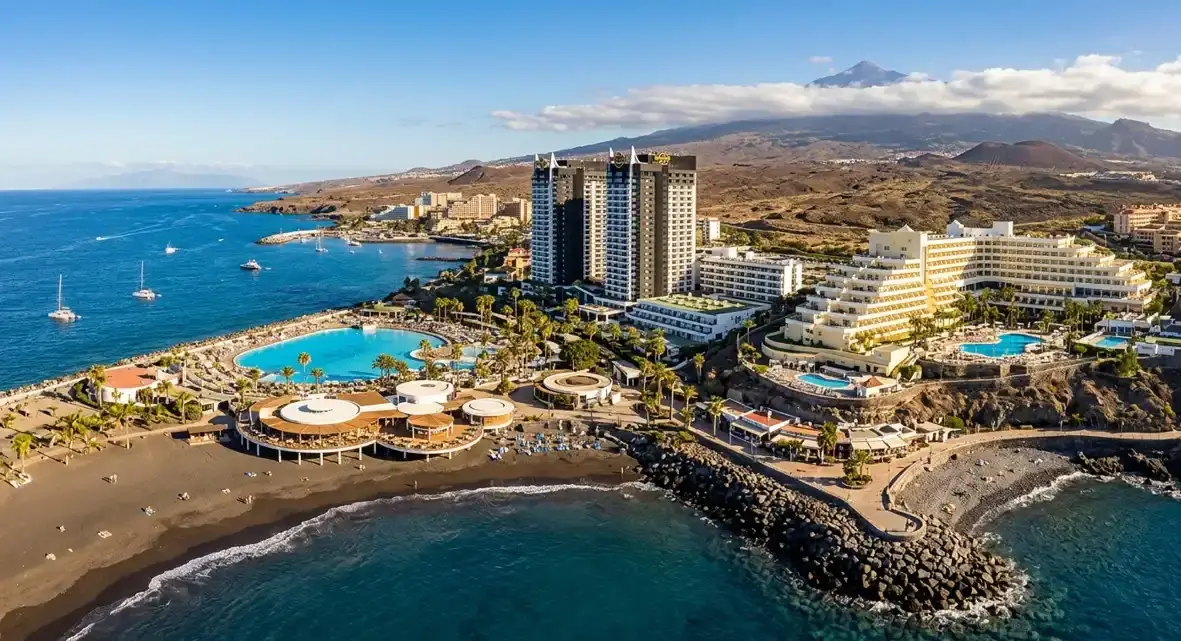 A modern view of Playa Paraiso resort in Tenerife, showcasing its luxury high-rise hotels, rocky coves, and oceanfront lidos for holidaymakers booking an affordable airport taxi transfer.