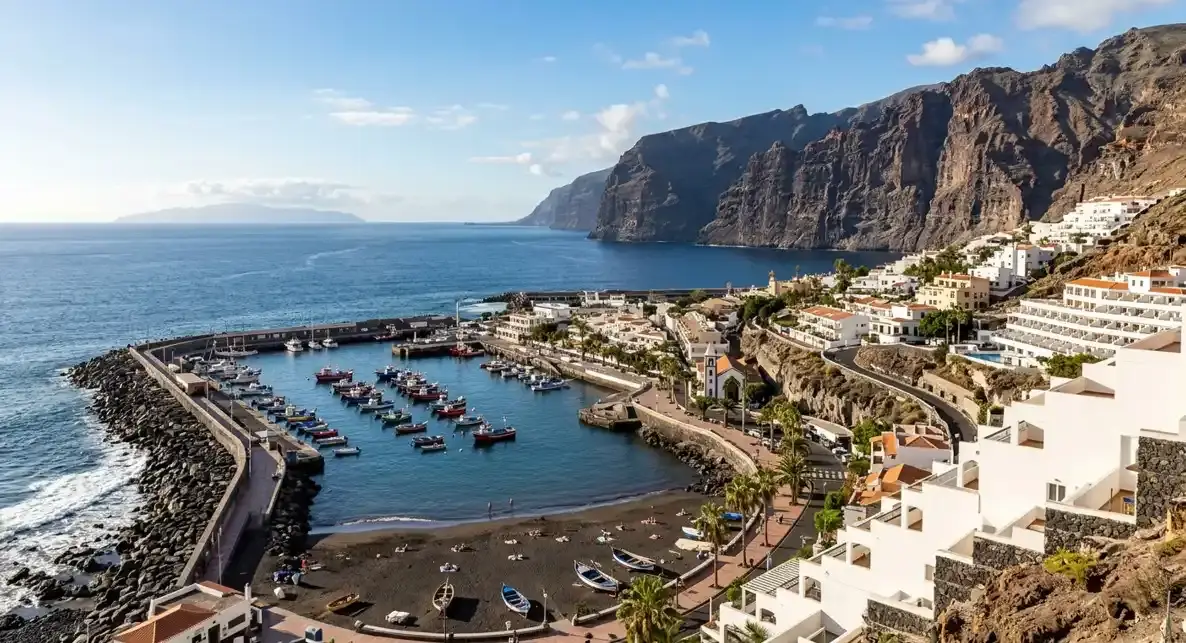 Private taxi arriving at the black sand resort of Puerto de Santiago near Los Gigantes cliffs, highlighting an affordable airport transfer where travelers pay the driver directly at their destination.